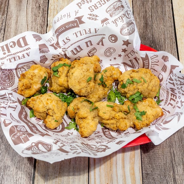 Golden-brown fried chicken nuggets, garnished with fresh cilantro, served in a red basket lined with patterned paper.