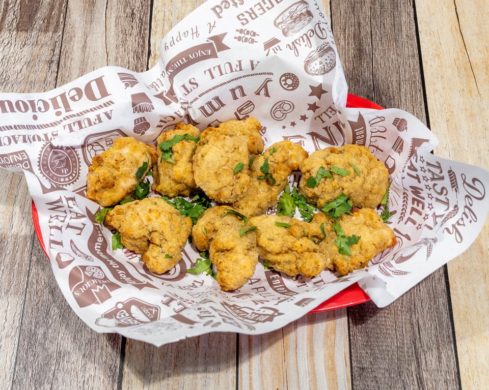 Golden-brown fried chicken nuggets, garnished with fresh cilantro, served in a red basket lined with patterned paper.