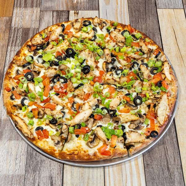 A whole pizza topped with chicken, black olives, mushrooms, tomatoes, and green onions.