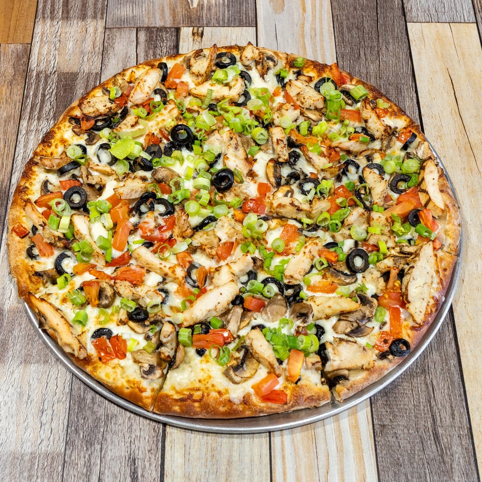 A whole pizza topped with chicken, black olives, mushrooms, tomatoes, and green onions.