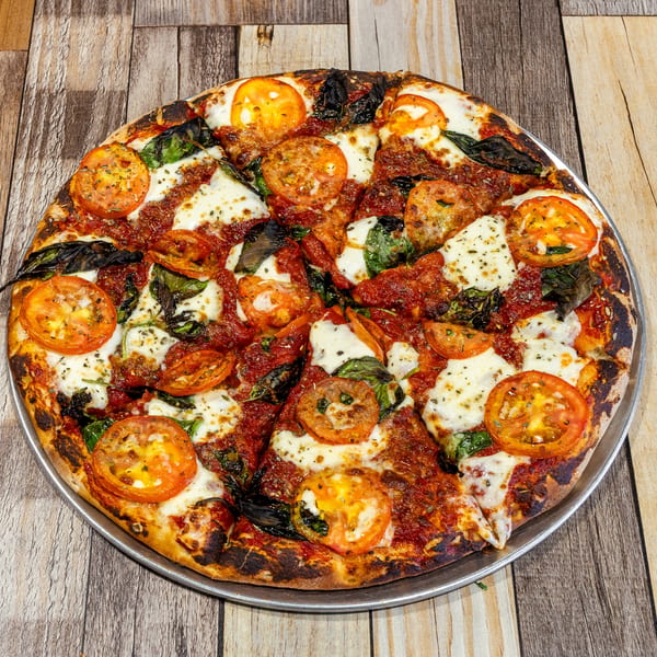 A freshly baked pizza with tomato slices, mozzarella cheese, and basil on a wooden table.