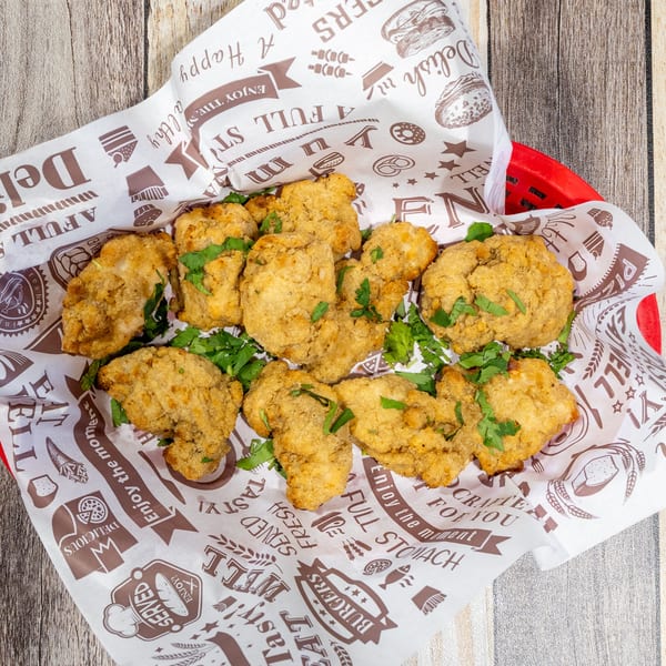 Crispy fried chicken bites with fresh parsley in a red basket lined with patterned paper.