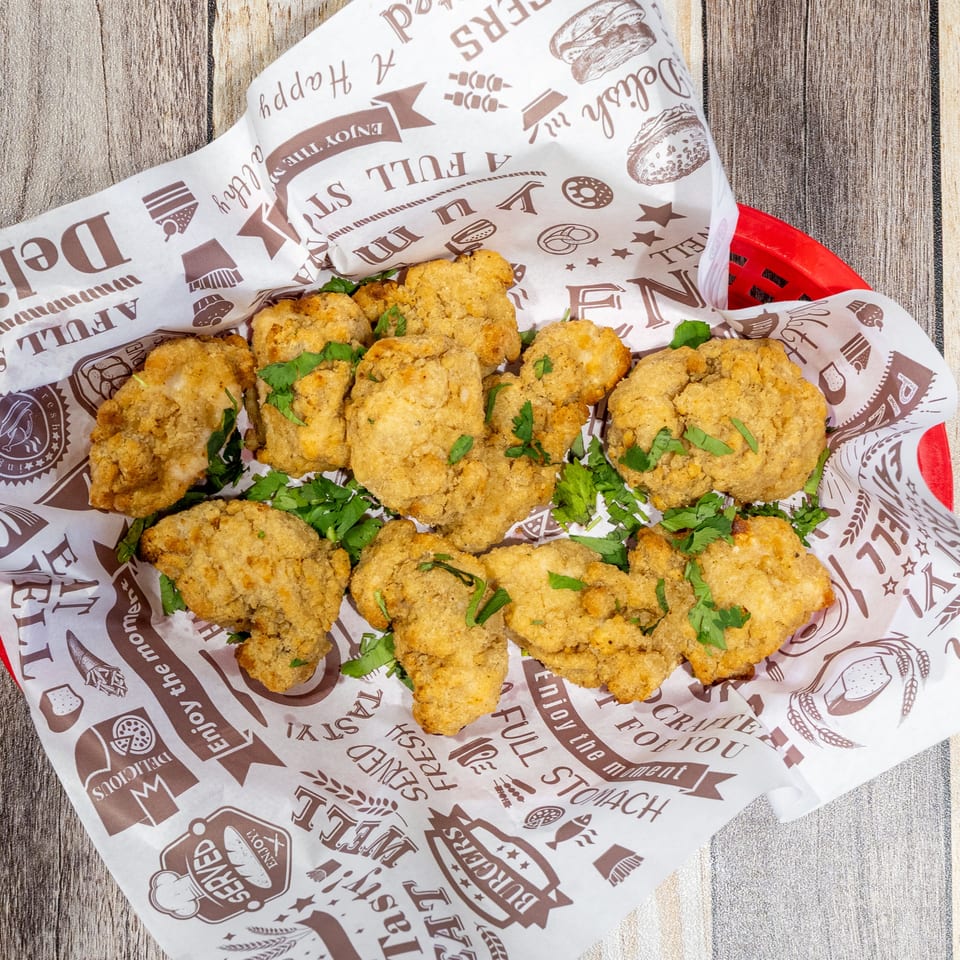 Crispy fried chicken bites with fresh parsley in a red basket lined with patterned paper.
