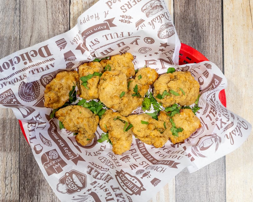 Crispy fried chicken bites with fresh parsley in a red basket lined with patterned paper.