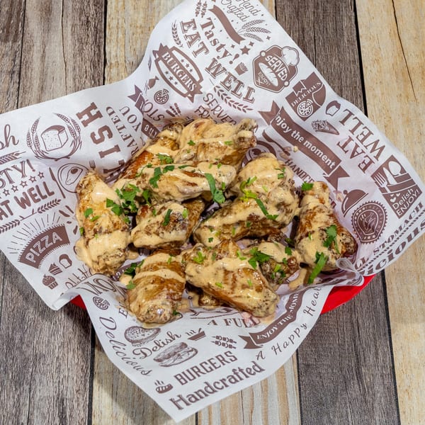 A basket of chicken wings coated in a creamy sauce and garnished with parsley, on a wooden table.