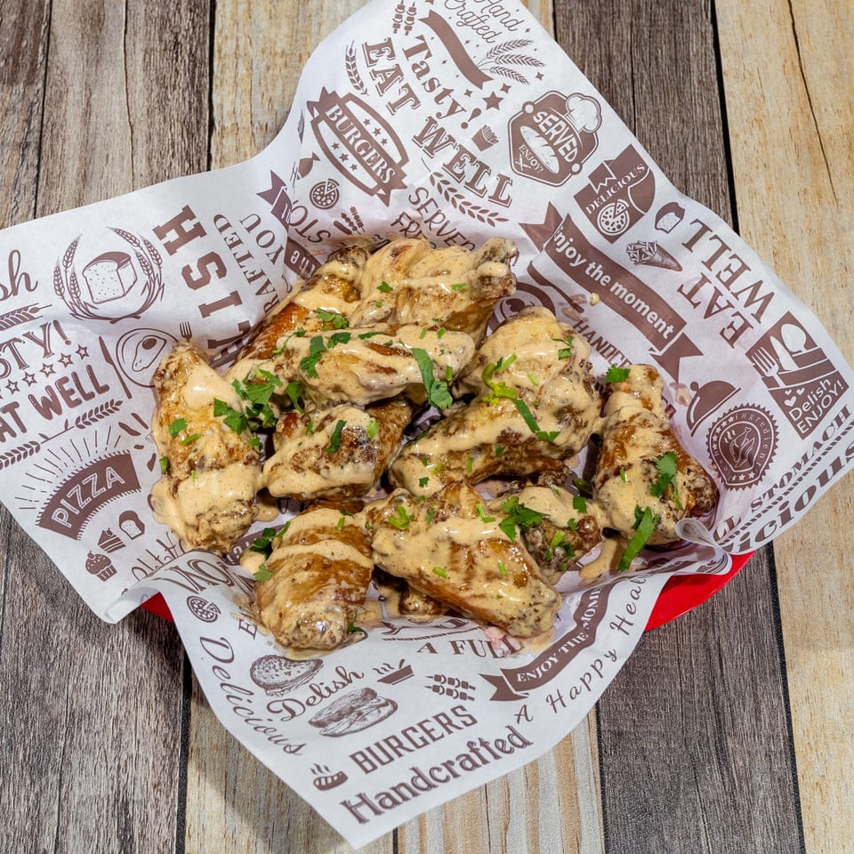 A basket of chicken wings coated in a creamy sauce and garnished with parsley, on a wooden table.