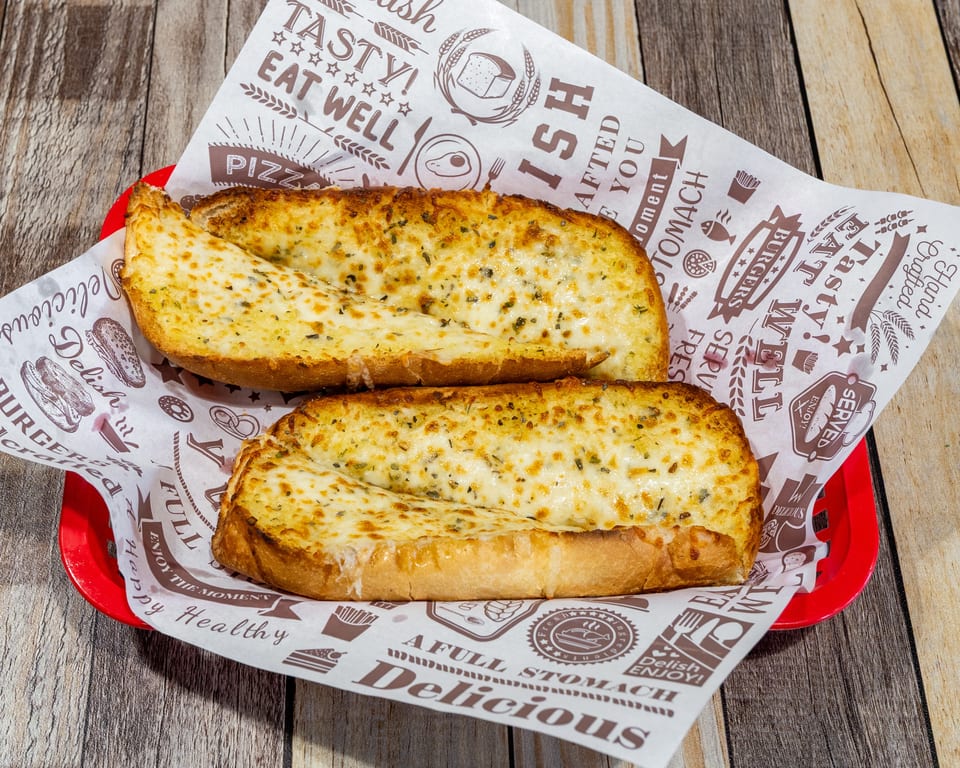 Two slices of cheesy garlic bread with herbs, served in a red basket lined with patterned paper.