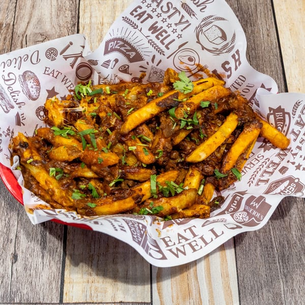 A red basket filled with golden french fries covered in a rich, savory sauce and fresh cilantro.