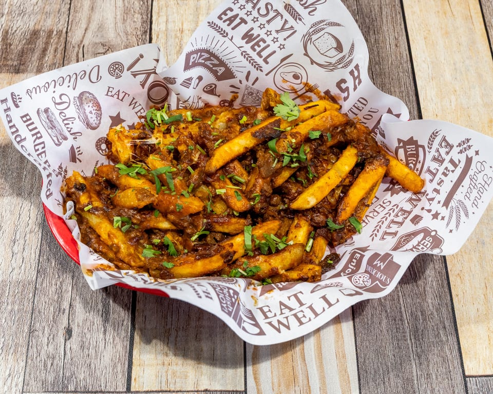 A red basket filled with golden french fries covered in a rich, savory sauce and fresh cilantro.