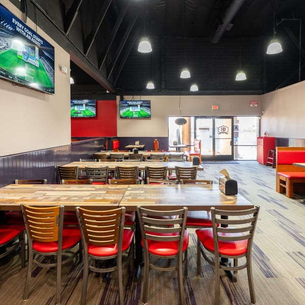 A restaurant dining room with wooden tables, red chairs, and TVs showing a soccer game.