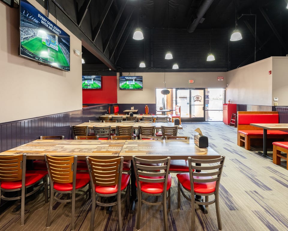 A restaurant dining room with wooden tables, red chairs, and TVs showing a soccer game.