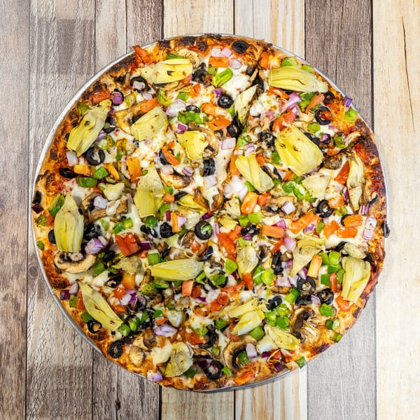 Overhead view of a vibrant veggie pizza with artichokes, olives, mushrooms, and peppers on a wooden table.