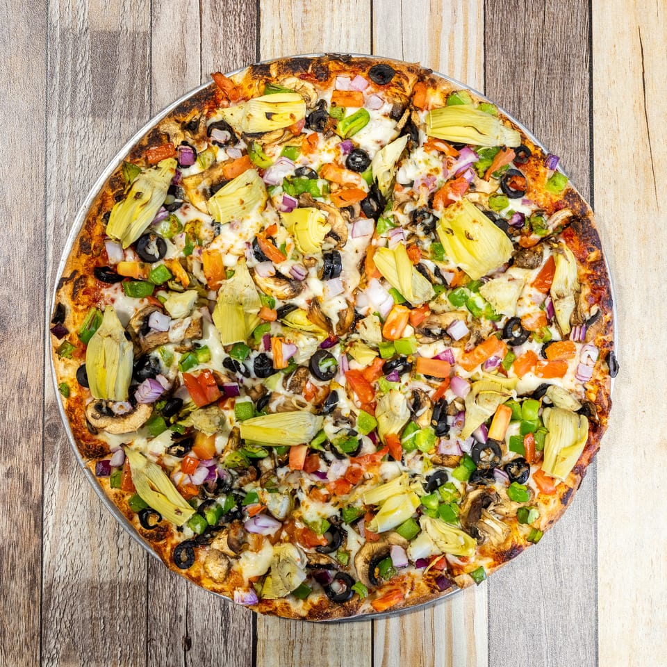 Overhead view of a vibrant veggie pizza with artichokes, olives, mushrooms, and peppers on a wooden table.