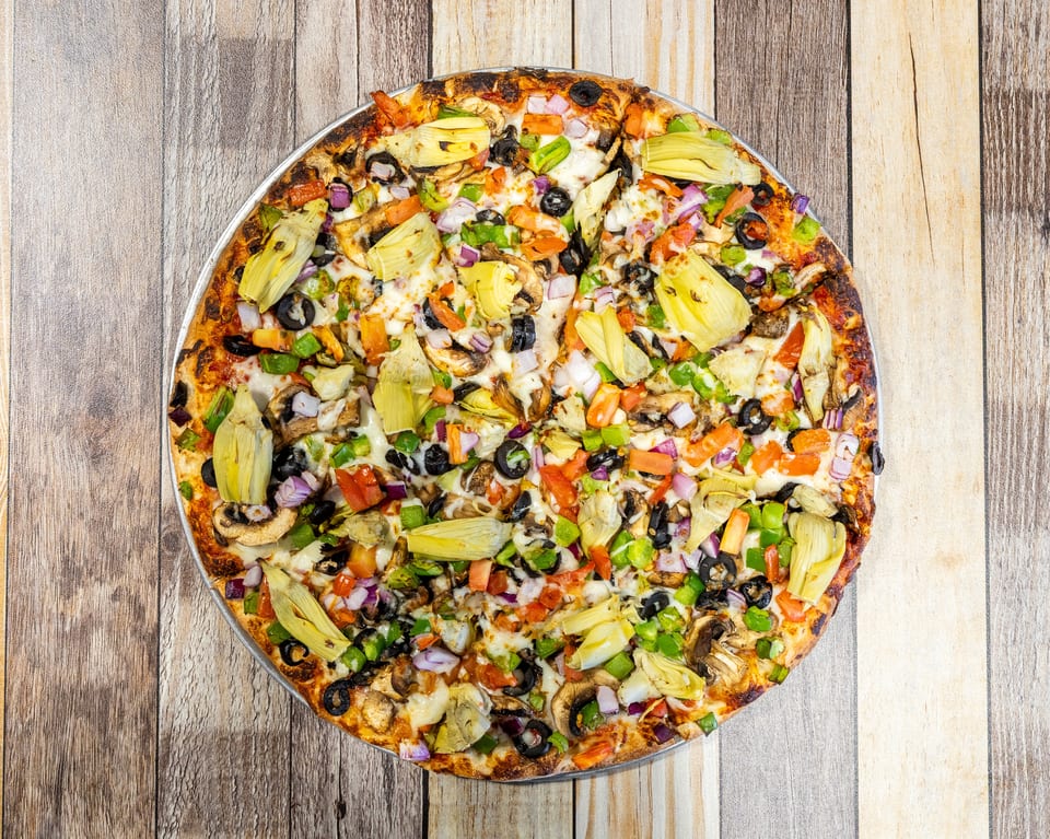 Overhead view of a vibrant veggie pizza with artichokes, olives, mushrooms, and peppers on a wooden table.