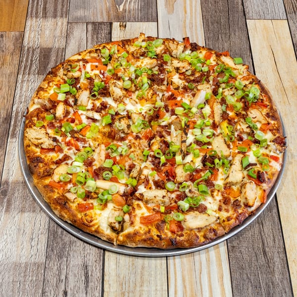 A whole chicken bacon ranch pizza, topped with green onions, on a wooden table.