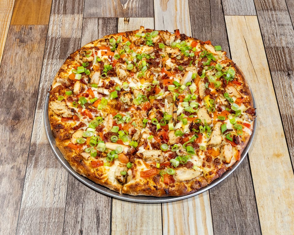 A whole chicken bacon ranch pizza, topped with green onions, on a wooden table.