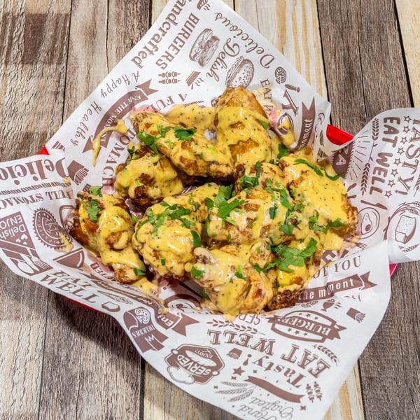 A basket of crispy chicken wings covered in a creamy yellow sauce and fresh green herbs.