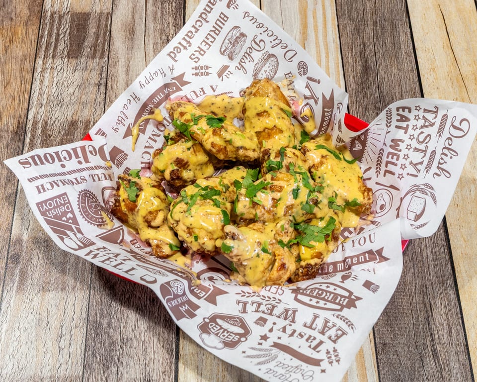 A basket of crispy chicken wings covered in a creamy yellow sauce and fresh green herbs.