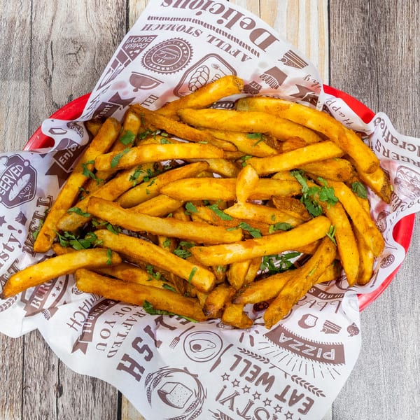 A red basket filled with golden french fries, seasoned with spices and fresh green herbs.