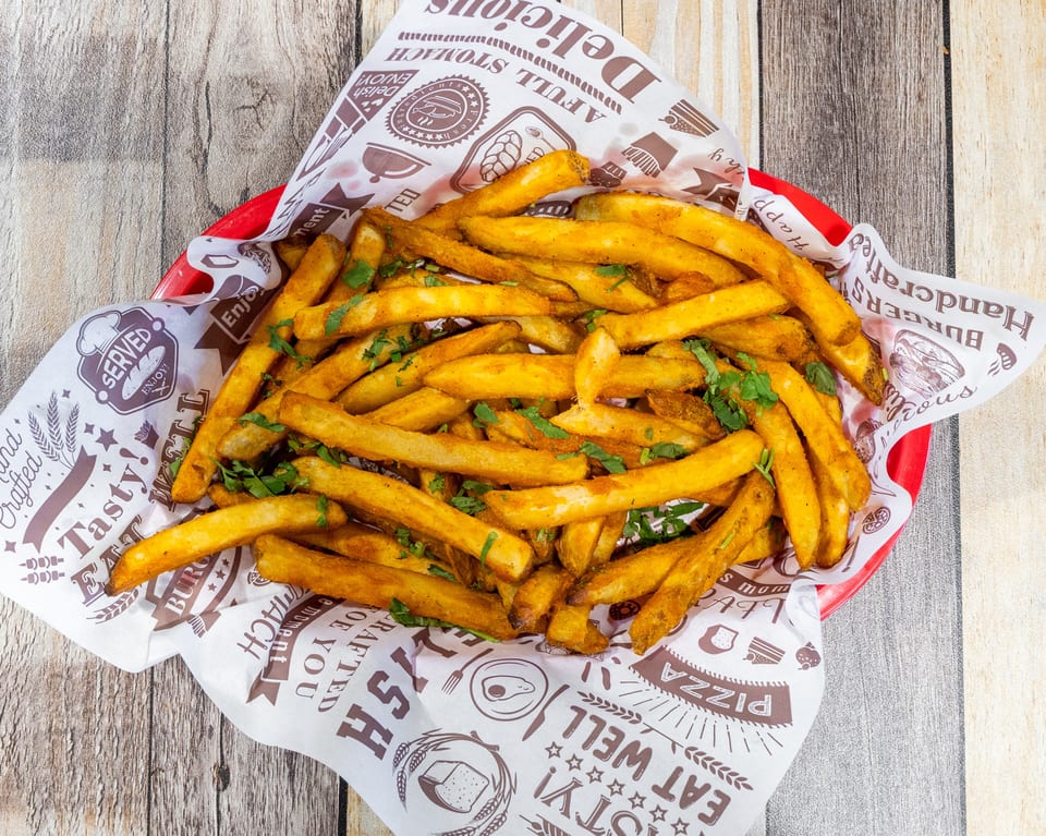 A red basket filled with golden french fries, seasoned with spices and fresh green herbs.