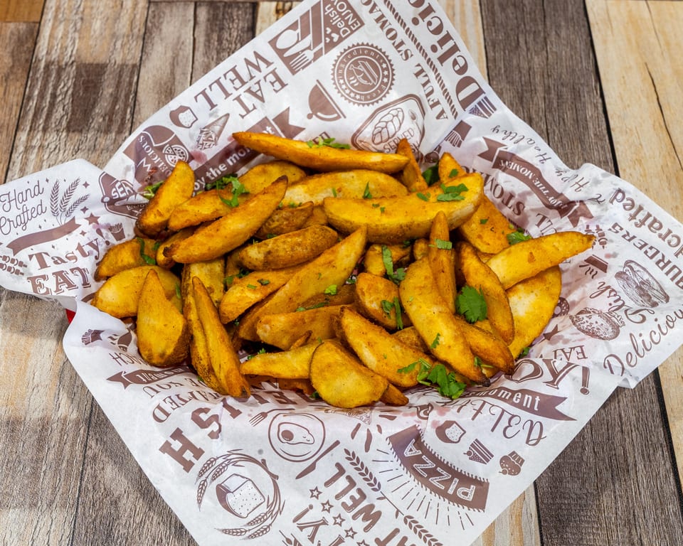 Golden potato wedges sprinkled with fresh herbs, served in a paper-lined basket on a wooden table.