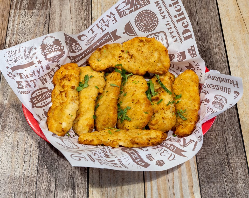 Golden-brown fried chicken tenders and nuggets, garnished with parsley, served in a red basket with patterned paper.
