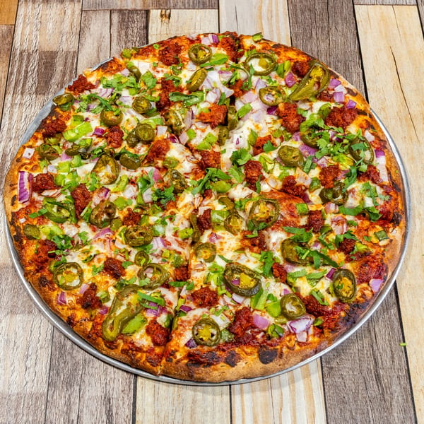 A whole pizza with chorizo, jalapeños, red onions, green peppers, and cilantro on a wooden table.