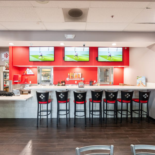 A modern bar area with red walls, multiple TVs, beer taps, and red-seated bar stools.