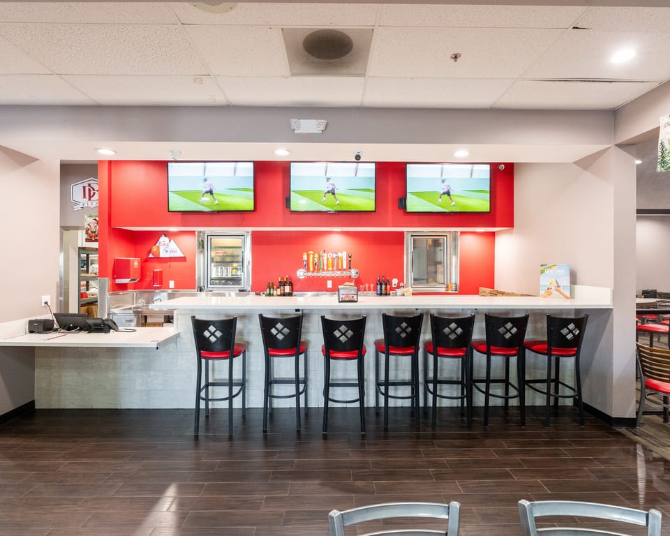 A modern bar area with red walls, multiple TVs, beer taps, and red-seated bar stools.