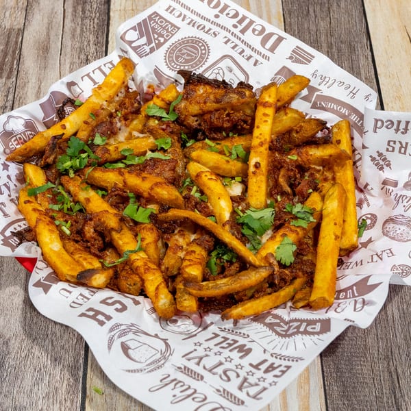 Golden seasoned fries topped with savory meat and fresh cilantro, served in a paper-lined basket.