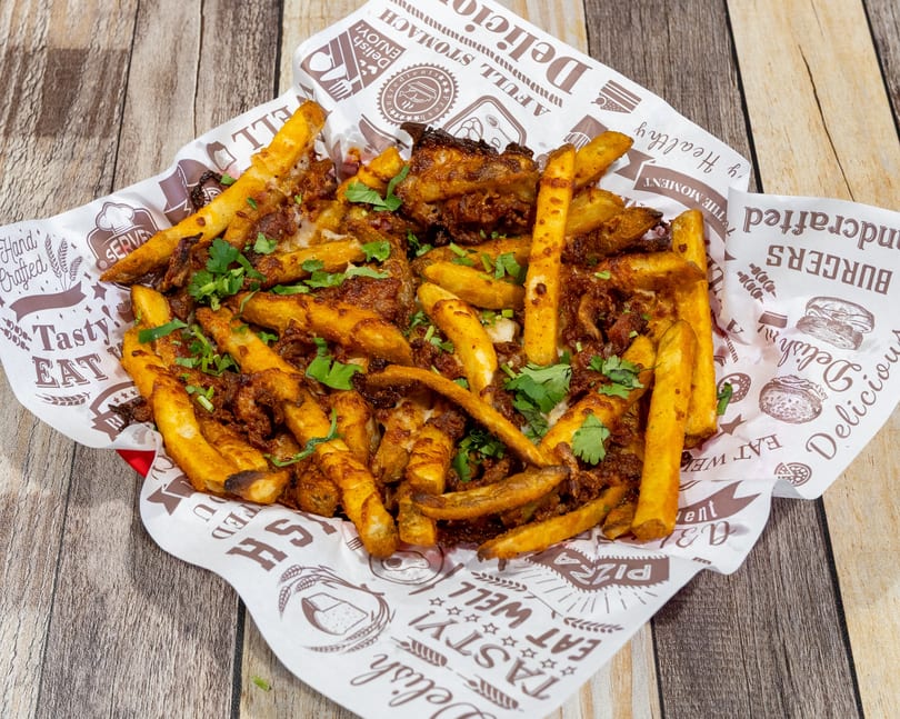 Golden seasoned fries topped with savory meat and fresh cilantro, served in a paper-lined basket.