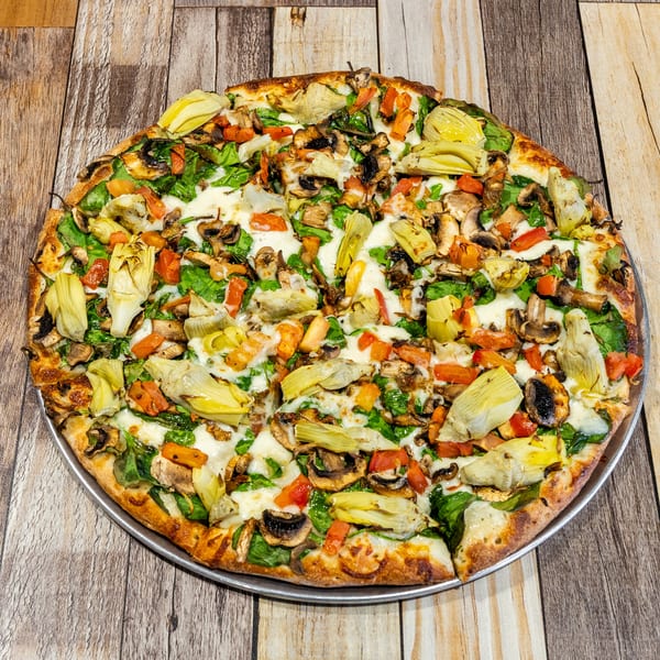 Whole vegetarian pizza with artichokes, mushrooms, spinach, and tomatoes on a wooden table.