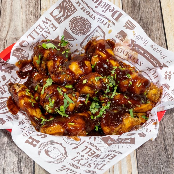 A basket of barbecue chicken wings, drizzled with sauce and garnished with fresh herbs.