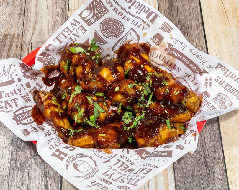 A basket of barbecue chicken wings, drizzled with sauce and garnished with fresh herbs.