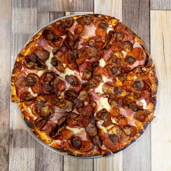 A whole meat lover's pizza with pepperoni, sausage, and ham on a wooden table.