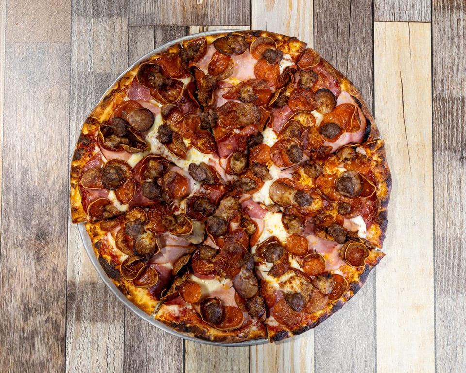 A whole meat lover's pizza with pepperoni, sausage, and ham on a wooden table.