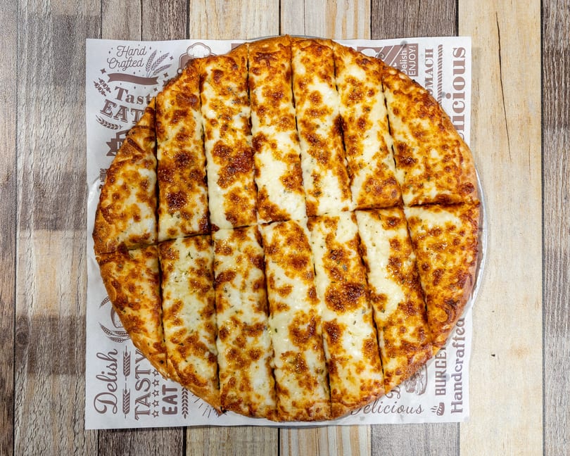 Golden brown cheesy breadsticks, cut into strips, served on branded parchment paper on a wooden table.