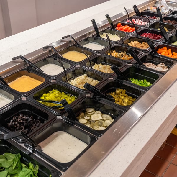 A salad bar with various toppings, dressings, and ingredients in black containers.